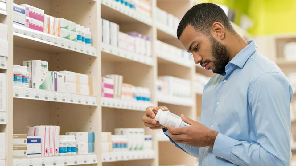 A man in a blue shirt holding a bottle of probiotic supplements as he stands in front of a shelf full of similar products